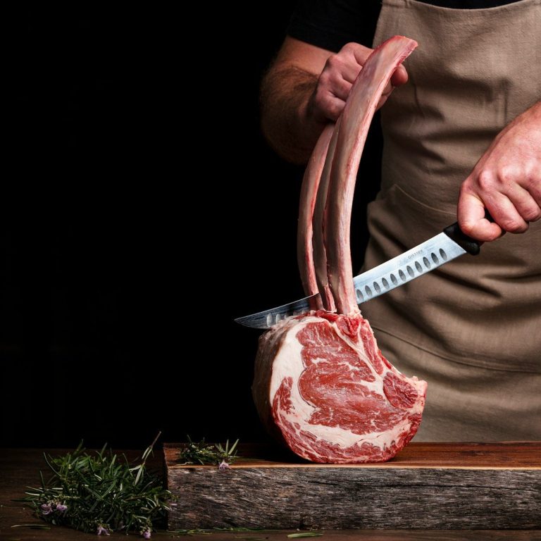 Un boucher tranche une côte de bœuf sur une planche en bois.