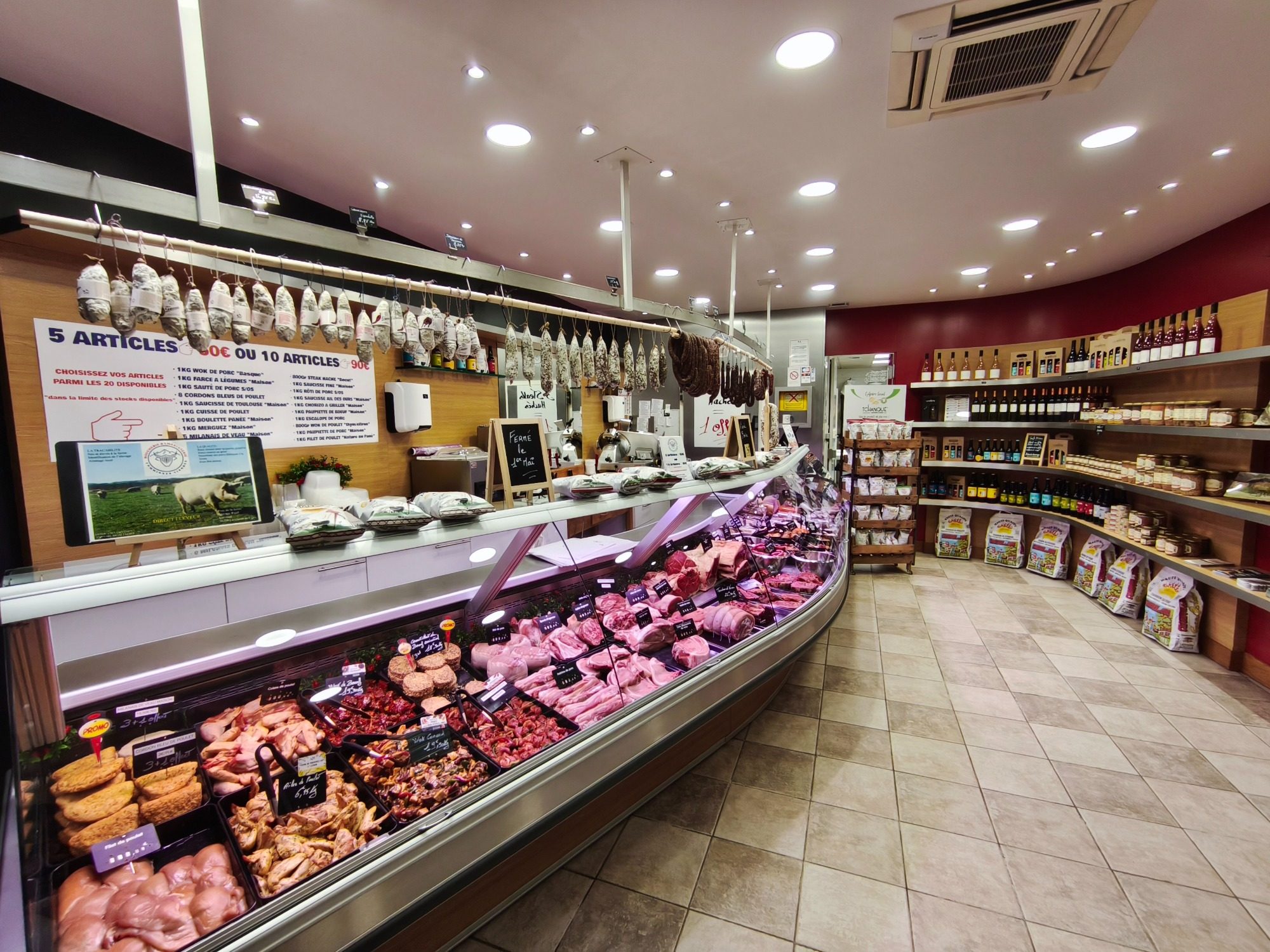 Boucherie moderne avec diverses viandes et produits locaux en vitrine.